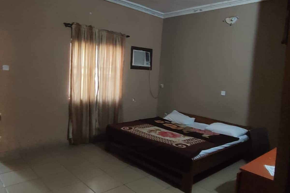 A bedroom with a bed, curtains, a clock, and a small table.