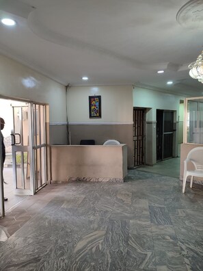 A reception area with a marble floor, a reception desk, a chair, and a framed artwork on the wall. - All Saints House (Abuja)