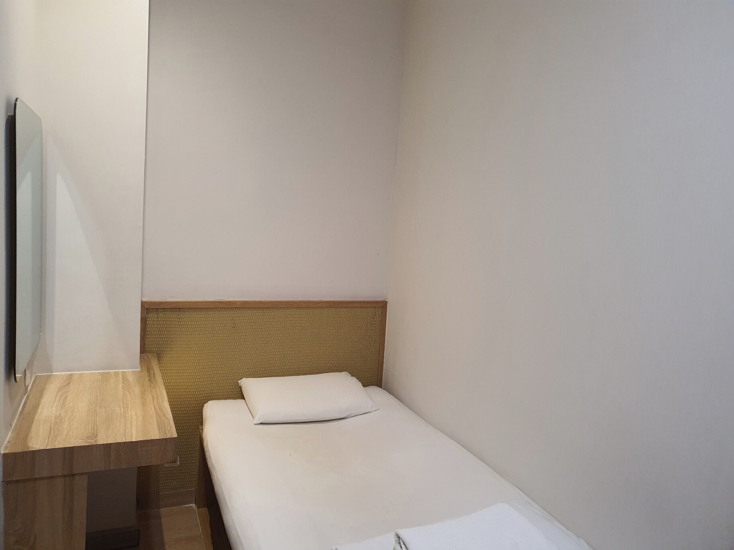 A small, single-bed room with a wooden headboard, a wooden nightstand, and a mirror on the wall.