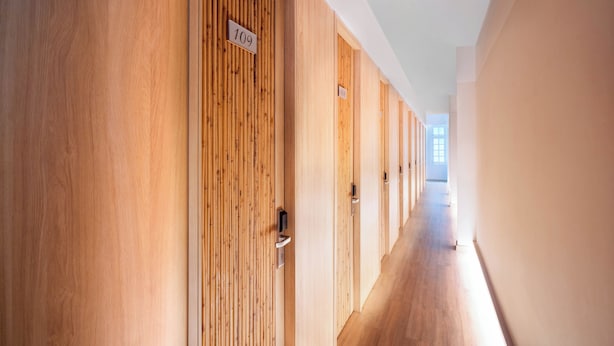A hallway with wooden paneling and numbered doors, leading to individual rooms. - Grandma Lu's Saigon Japan Town (Ho Chi Minh City)