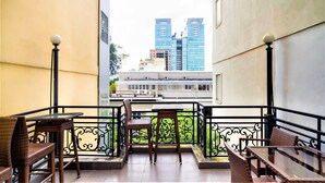 A balcony with wicker furniture and a glass table, overlooking a cityscape with modern buildings. - Grandma Lu's Saigon Japan Town (Ho Chi Minh City)