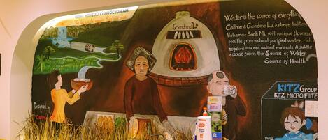 A wall mural with a water-themed design, a small counter with a bottle of lotion, and a computer monitor.