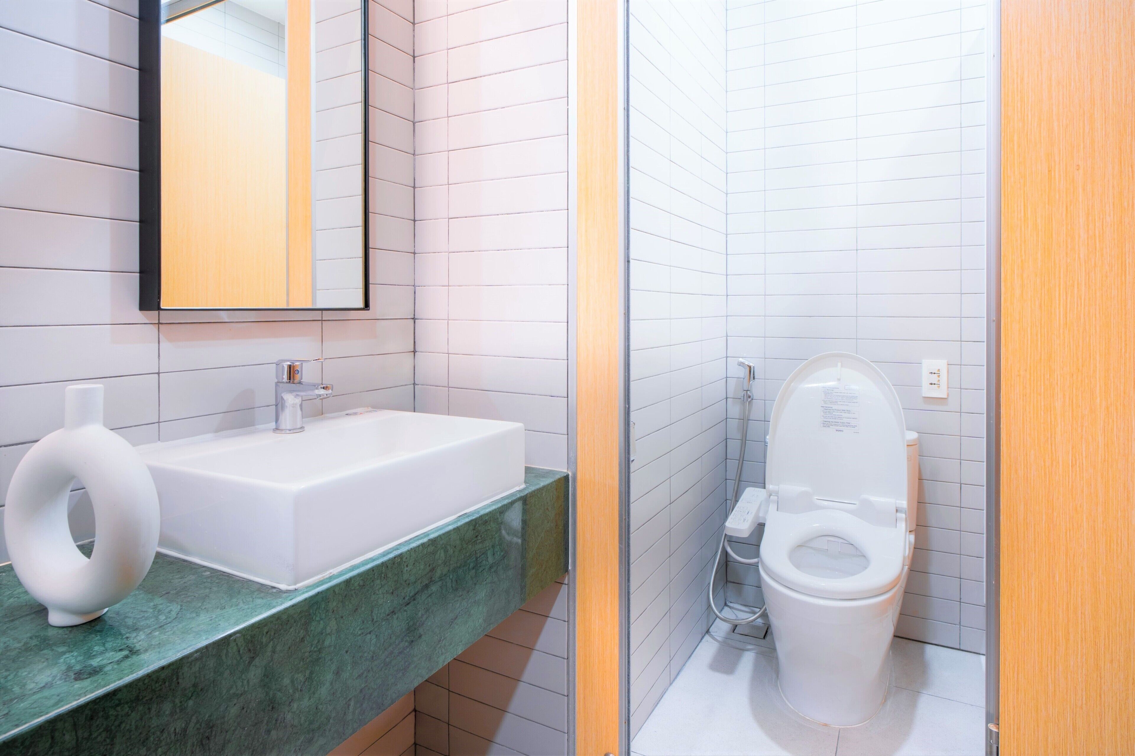 A modern bathroom with a white sink, a mirror, and a toilet.