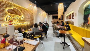 A restaurant interior with brick walls, hanging lights, and a yellow bench area. - Grandma Lu's Saigon Japan Town (Ho Chi Minh City)