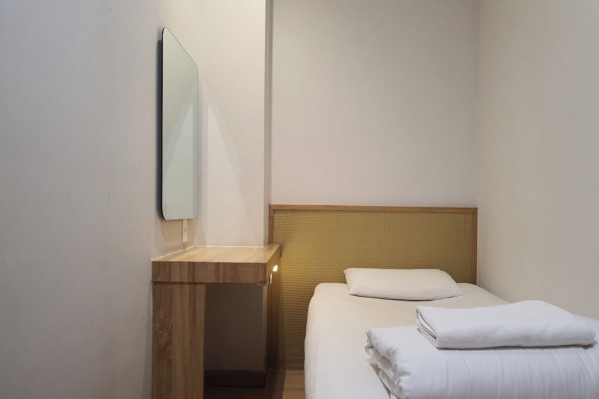 A small, clean hotel room with a single bed, a wooden nightstand, and a mirror.