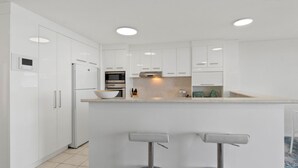 A modern kitchen with white cabinetry, a central island with a bowl, and a bar area with stools.