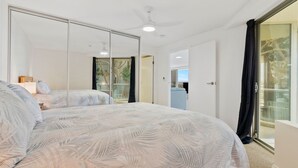 A bedroom with a large bed, a ceiling fan, and a sliding glass door leading to a balcony.