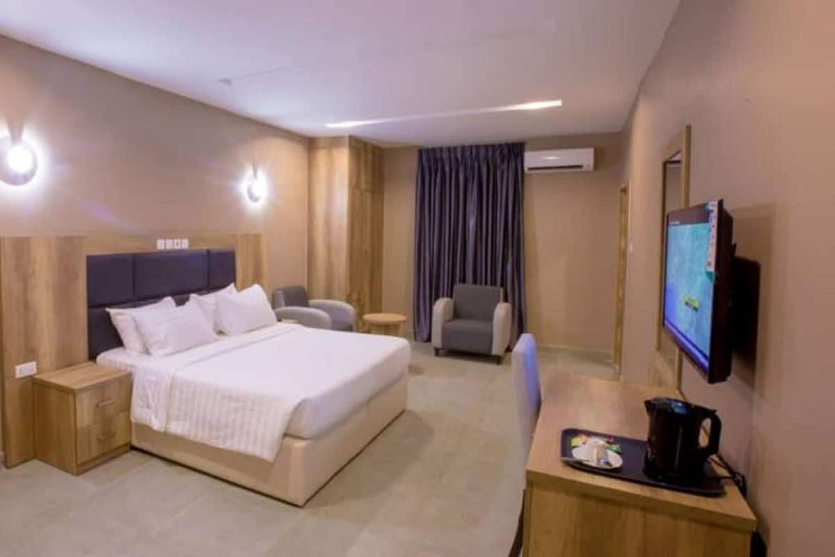 A hotel room with a bed, bedside tables, a desk with a chair, a TV, and a window with curtains.