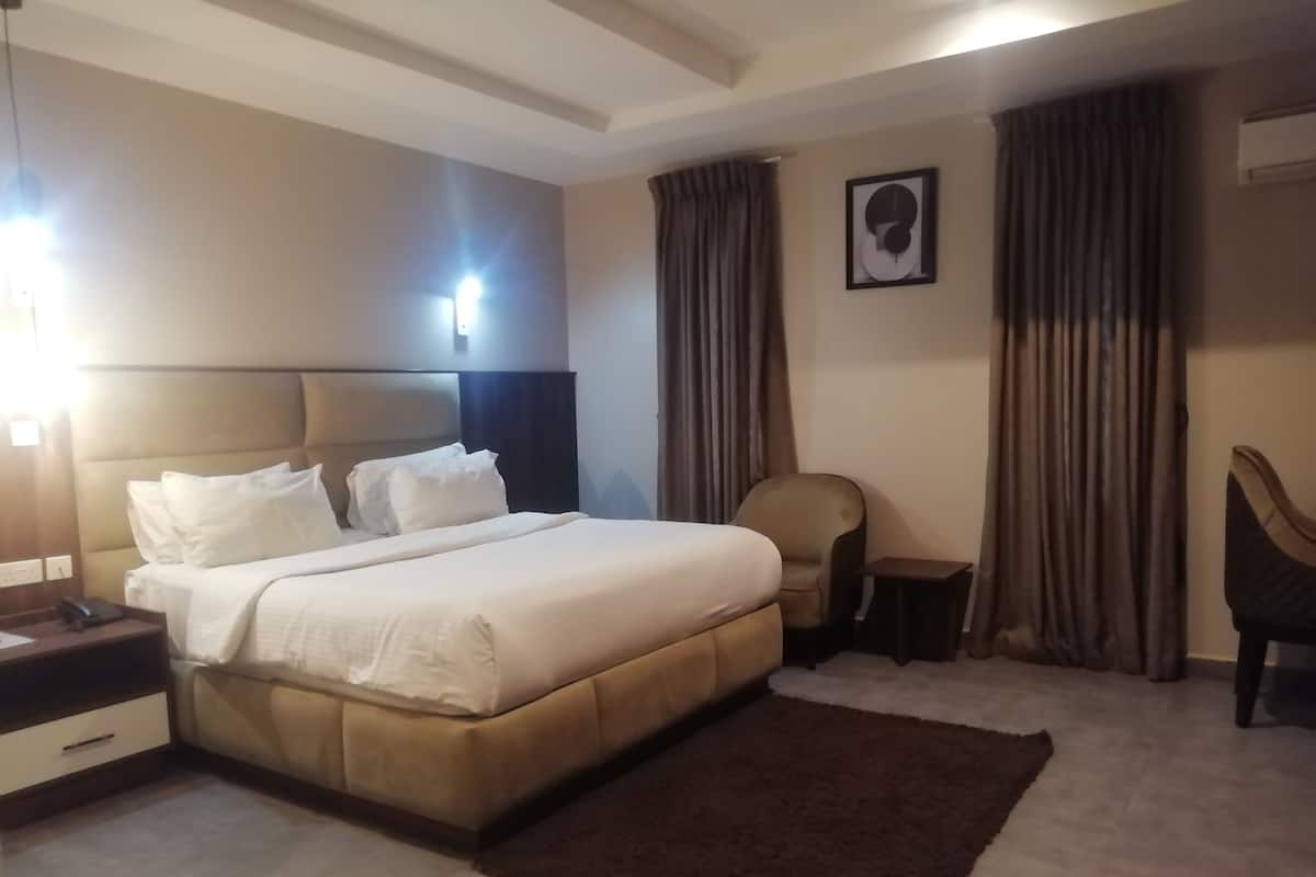 A hotel room with a large bed, a chair, a small table, and a wall-mounted light.