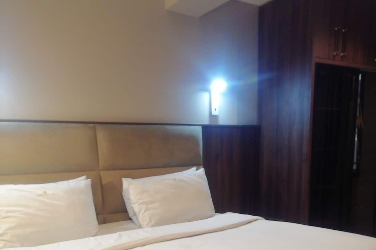 A large bed with a headboard, two pillows, and a light source on the wall.