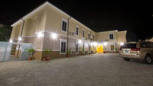 A two-story building with a paved driveway and a parked car. - Ivana Residence Apartments and Suites (Abuja)