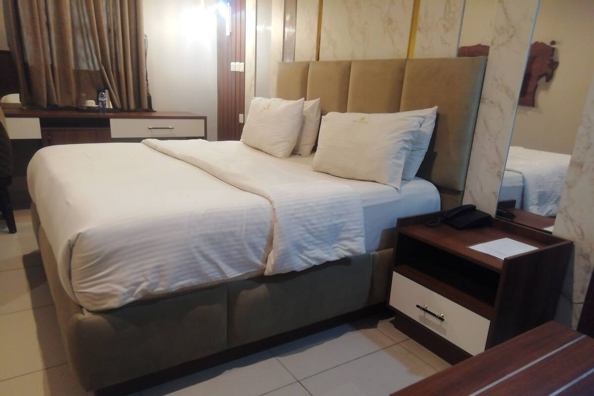 A hotel room with a large bed, bedside tables, a desk, and a mirror.