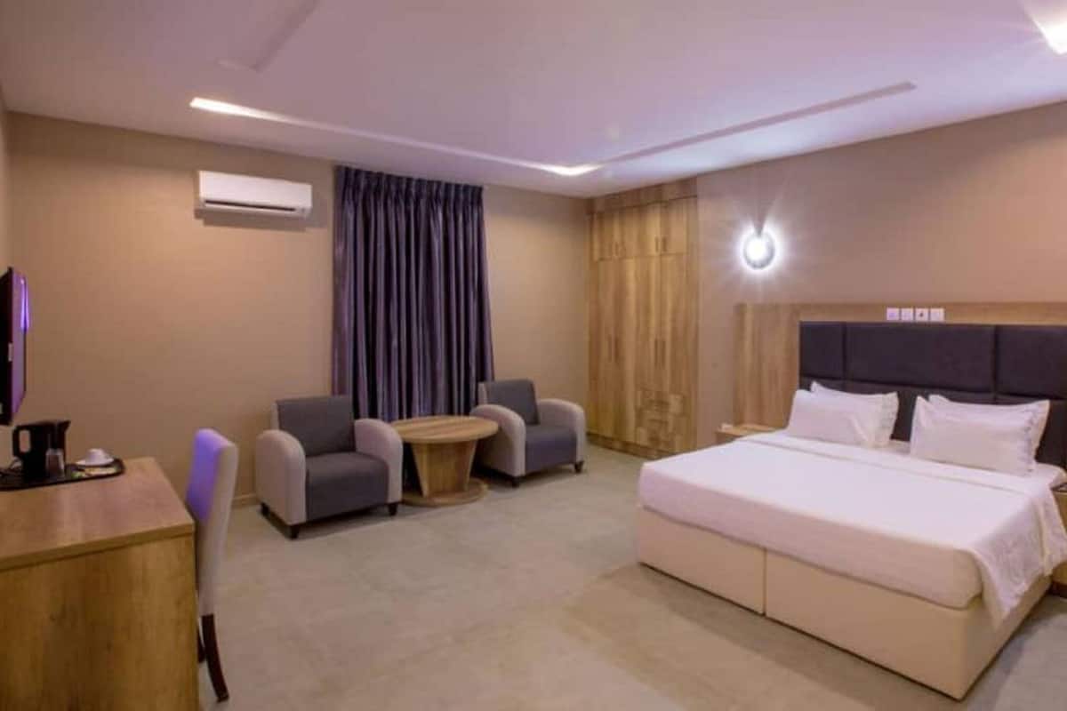 A hotel room with a large bed, two armchairs, a small round table, and a desk with a coffee maker.