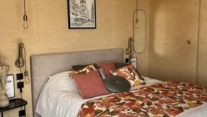 A bedroom with a bed, a ceiling fan, a framed picture on the wall, and a bedside table with a lamp. - Cabane Insolite L'alrance (Bozouls)