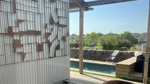 A covered outdoor area with a pool, a stone wall, and a wooden deck. - Cabane Insolite L'alrance (Bozouls)