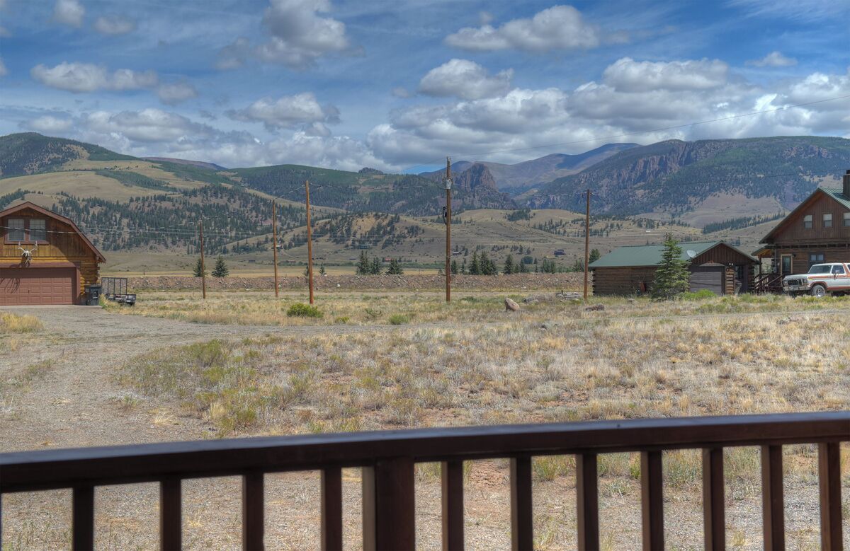 A rustic cabin with a gravel driveway, surrounded by mountains and sparse vegetation.