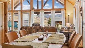 Ein gemütlicher Essbereich mit Holztisch, Ledersesseln und Bergblick durch große Fenster.