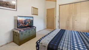 Ein Schlafzimmer mit einem Bett, einem Fernseher auf einem alten Koffer, einem Holzschrank und einem gerahmten Bild an der Wand.