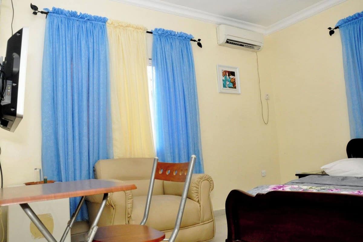 A room with a bed, a chair, a table, and curtains.