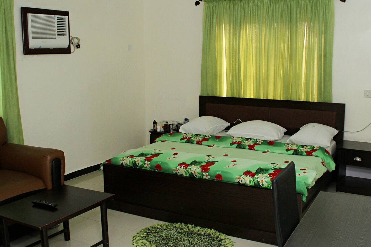 A bedroom with a bed, a chair, a bedside table, and a lamp.