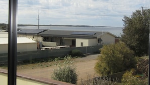 Vista costera con una casa que tiene paneles solares, un patio cercado y una playa al fondo.