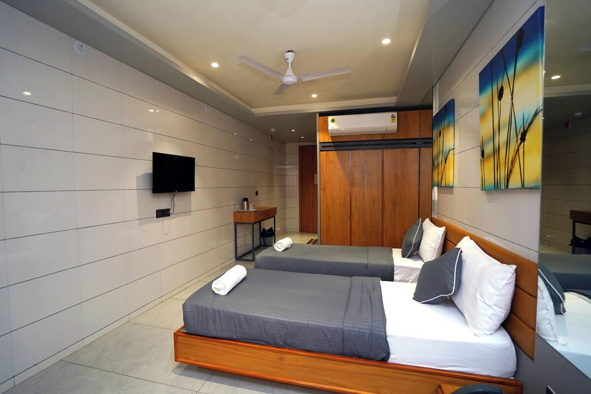 A hotel room with two beds, a flat-screen TV, a ceiling fan, and artwork on the wall.