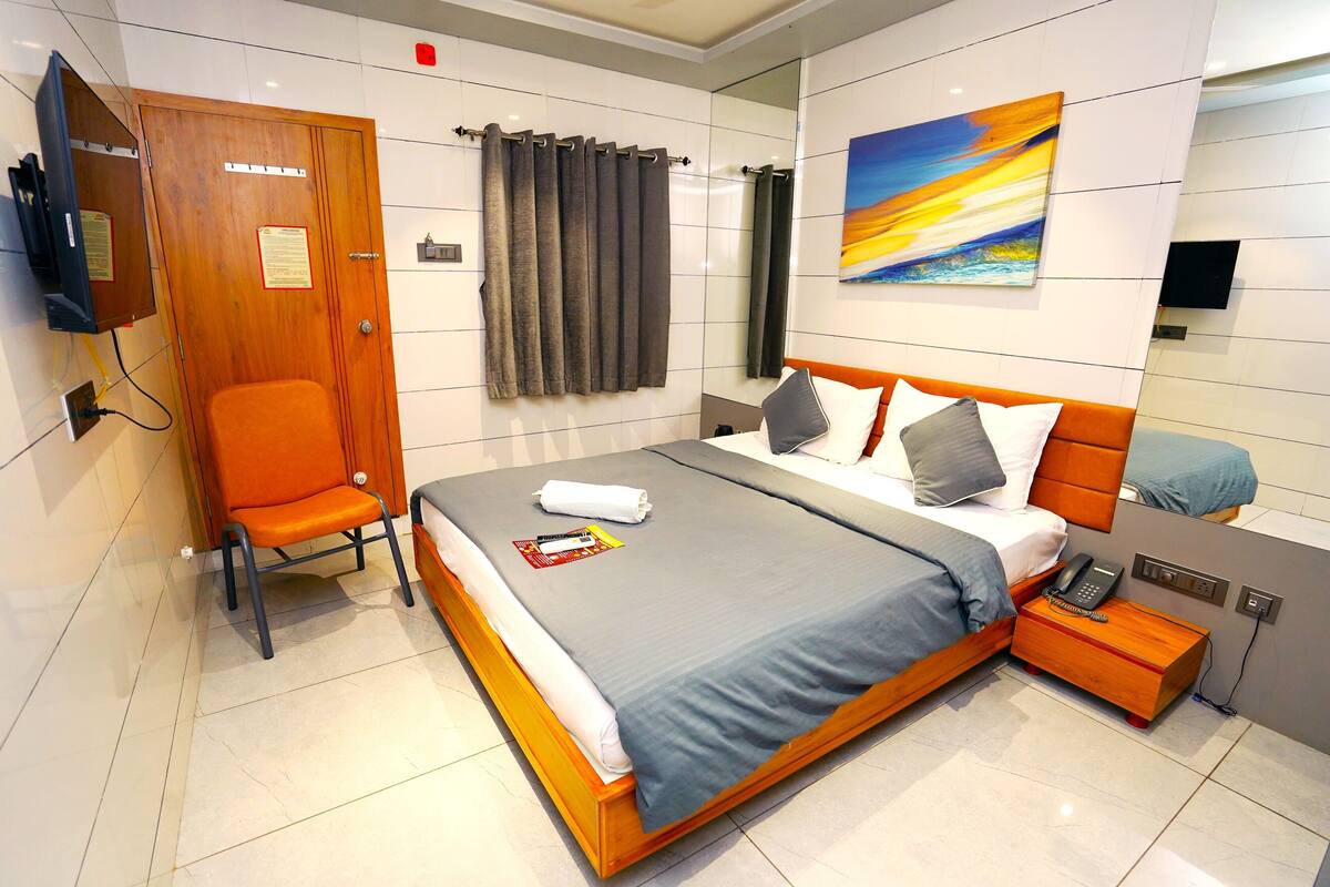 A modern hotel room with a large bed, a wooden nightstand, a chair, a television, and a painting on the wall.