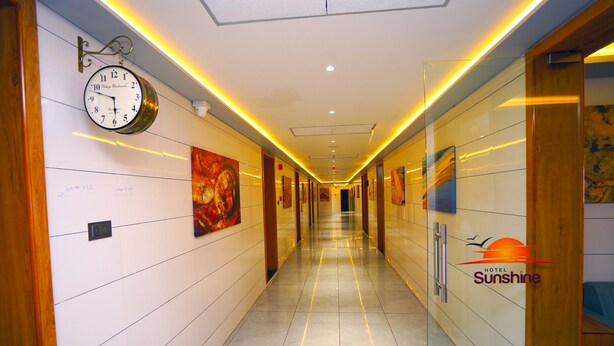 Ein Hotelkorridor mit einer Uhr, Kunstwerken an den Wänden und einem Schild für das 'Sunshine Hotel'.