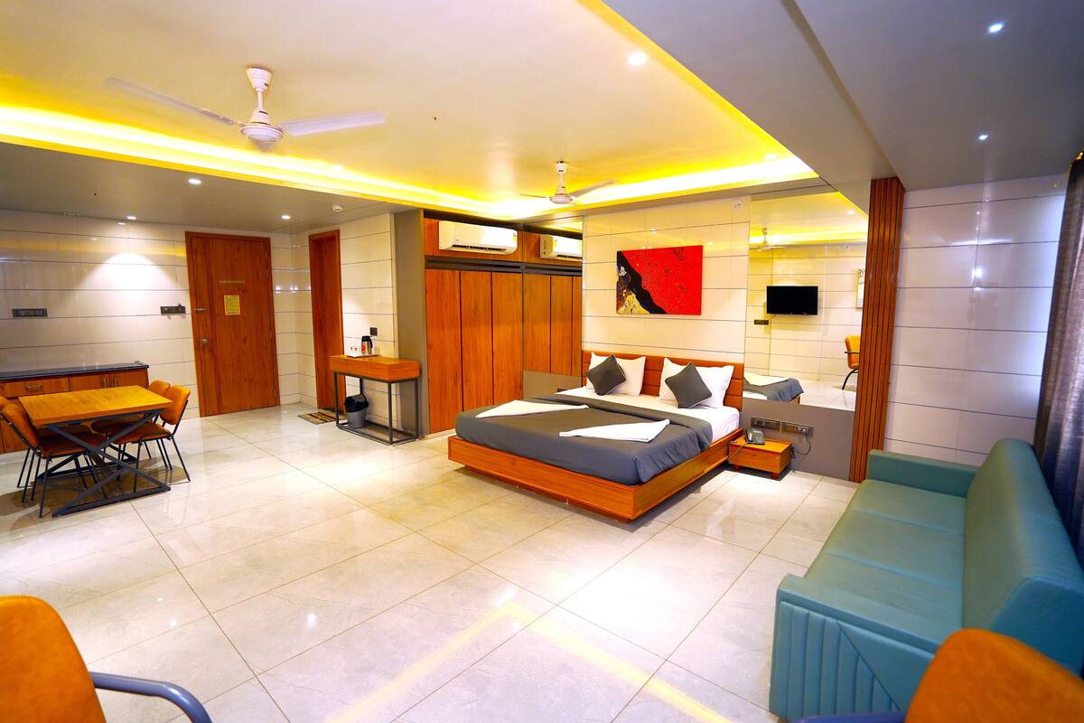A modern hotel room with a bed, a sofa, a dining table, and a TV.
