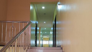 Un escalier avec une rampe en métal, menant à un couloir dont un des murs est peint en vert et qui se termine par une porte.