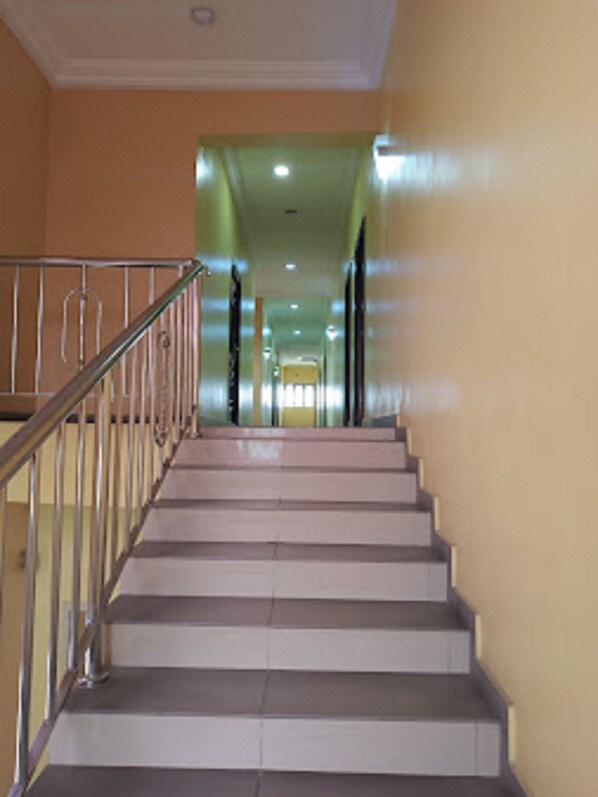 Un escalier avec une rampe en métal, menant à un couloir dont un des murs est peint en vert et qui se termine par une porte.