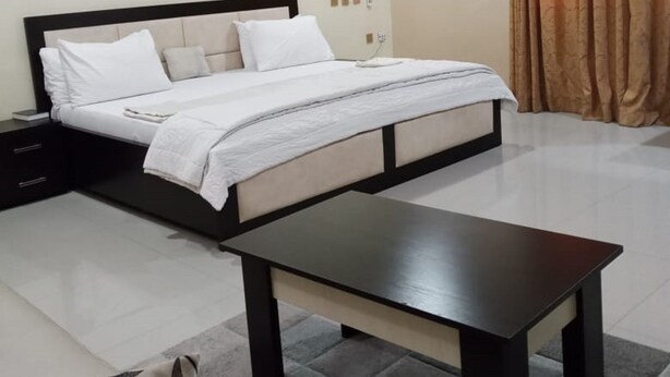 Une chambre à coucher comprenant un lit, des tables de chevet, une commode, une table basse en bois et une fenêtre avec des rideaux.
