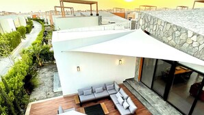 Un espacio exterior moderno con un muro de piedra, una terraza de madera y un paraguas grande.