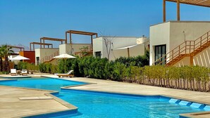 Un área de piscina moderna con varias piscinas, sillones de descanso y una pérgola de madera.