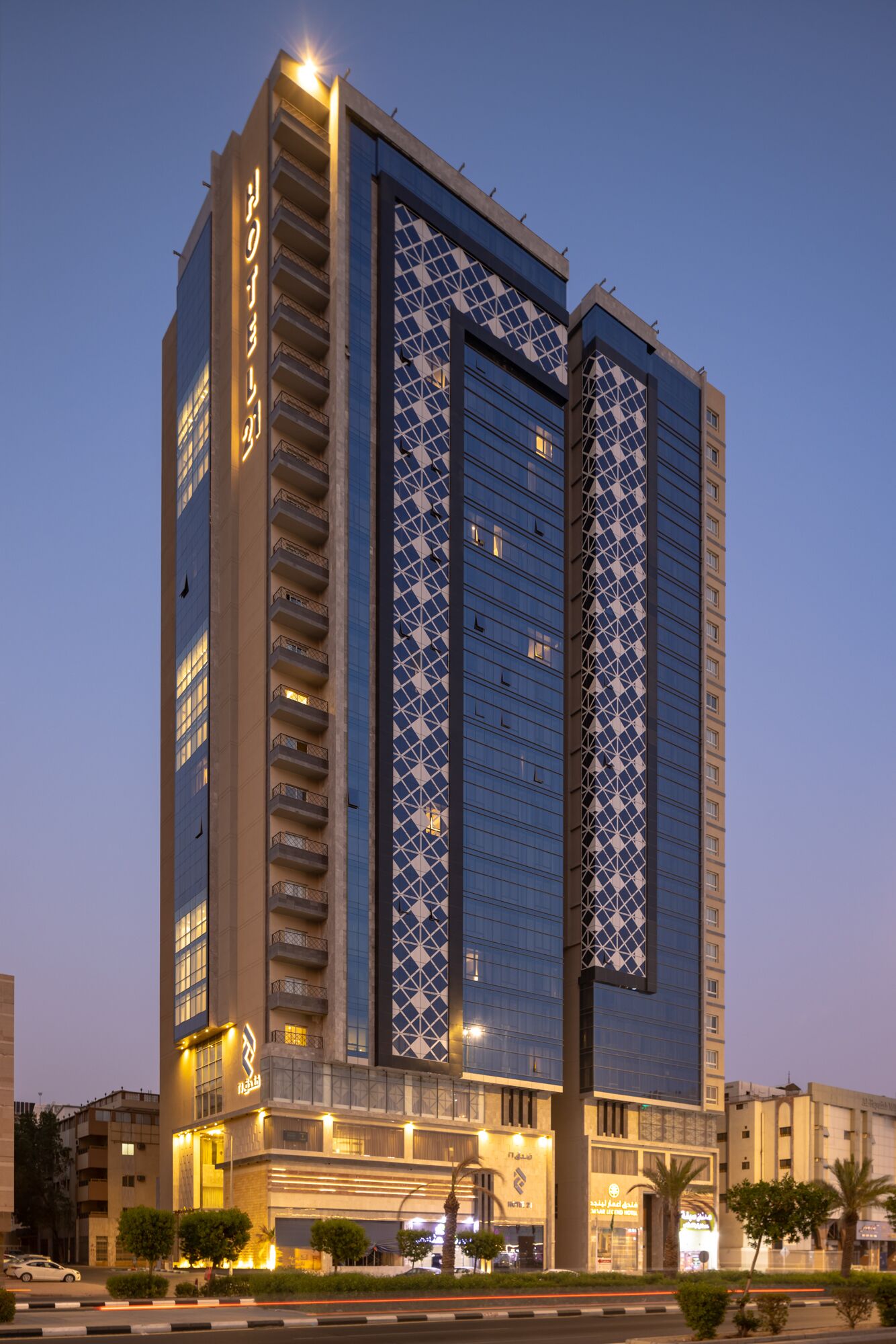 Un hotel moderno de gran altura con una fachada geométrica distintiva, varios balcones e iluminación de señalización.