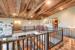 A spacious loft-style room with a high ceiling, exposed wooden beams, a mezzanine level with a railing, and a kitchen area visible below. - Incredible Views from Spacious Hillside Lodge Access to Clubhouse w/ 2 Pools (Lead)