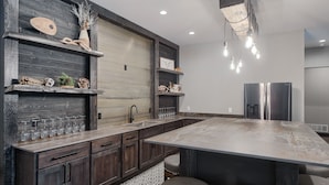 A modern kitchen with dark wood cabinetry, a large island, and a stainless steel refrigerator. - 6400+ Sq. Ft. Beautiful New Lodge in Powder House Pass w/ Comm. Pool Access! (Lead)