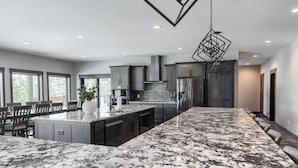 A modern kitchen with a large island, dark cabinetry, and a hanging light fixture. - 6400+ Sq. Ft. Beautiful New Lodge in Powder House Pass w/ Comm. Pool Access! (Lead)