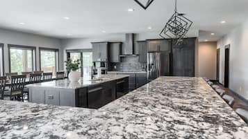 A modern kitchen with a large island, dark cabinetry, and a hanging light fixture.