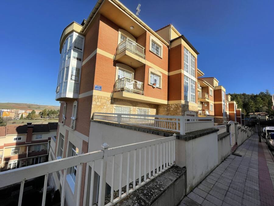A multi-story residential building with balconies, a stone facade, and a clear blue sky in the background.
