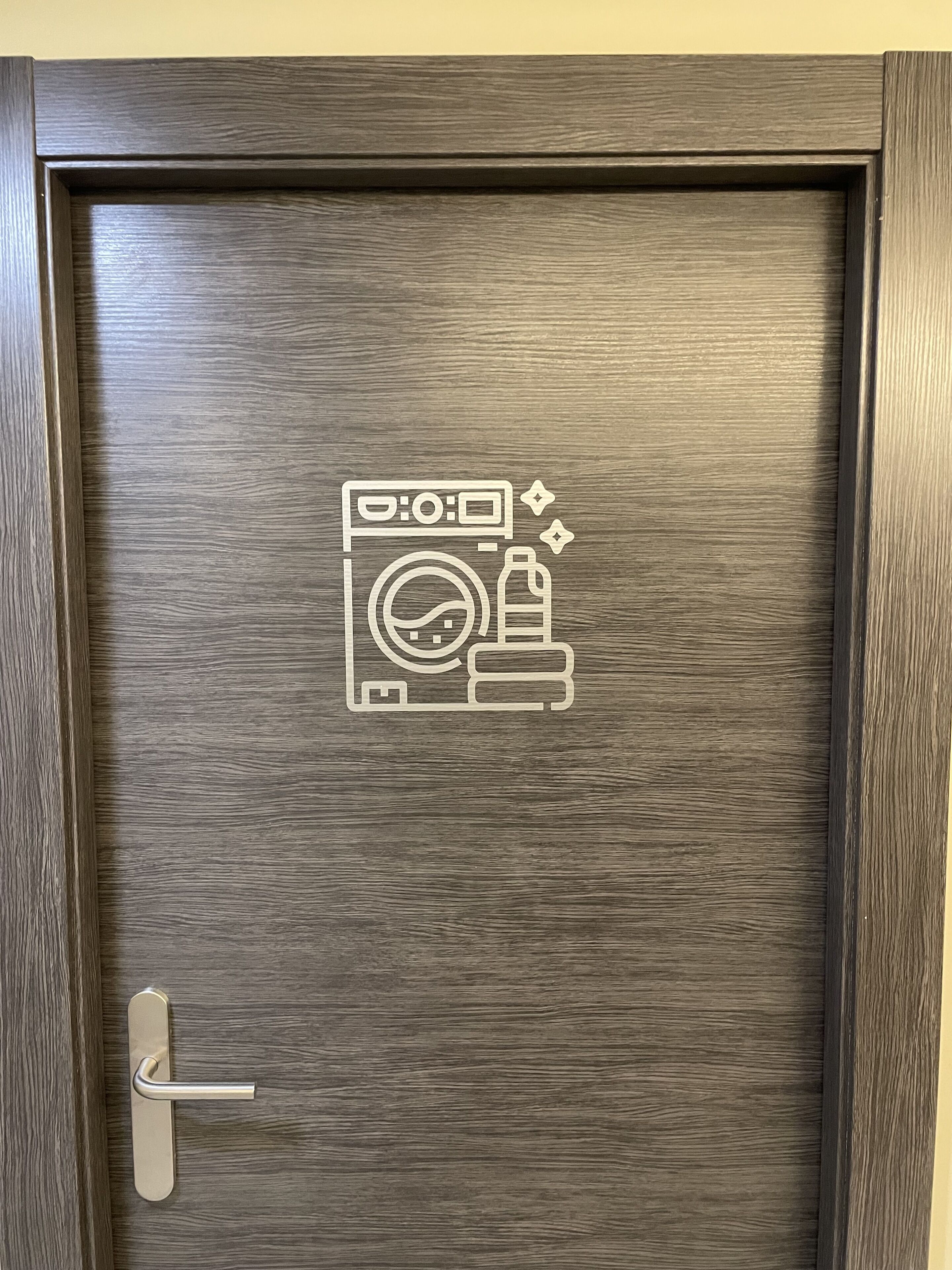 Una puerta de madera con un picaporte metálico y un símbolo de lavandería grabado en la superficie.