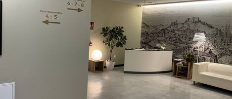 Un área de recepción con mostrador, una planta en maceta, un mural en la pared y señalización para los apartamentos.