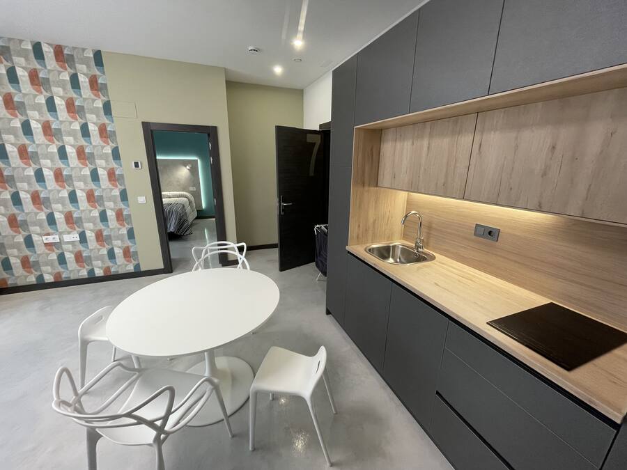 A modern kitchen with a built-in sink, dark cabinets, and a white dining table with chairs.