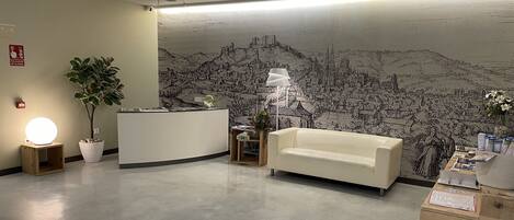 A reception area with a reception desk, a white sofa, a potted plant, a lamp, and a wall mural.