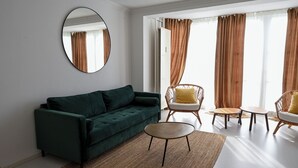 A modern living room with a dark green sofa, a round mirror, and a small coffee table. - 2 bedroom apartment in herrsching am ammersee (Herrsching am Ammersee)