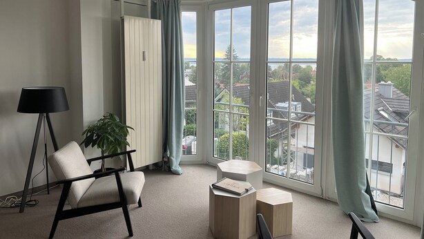 A modern living room with a large bay window, a floor lamp, a chair, and a side table. - 2 bedroom apartment in herrsching am ammersee (Herrsching am Ammersee)