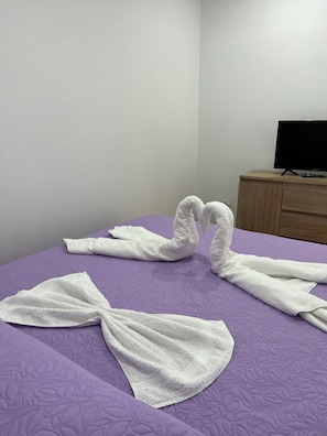 A hotel room with a purple bedspread, a wooden nightstand, and a television.