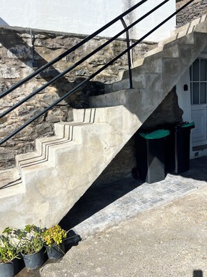 A concrete staircase with metal railings leading to a door, surrounded by stone walls and potted plants.