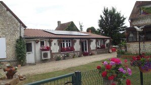 Ein Steinhaus mit Ziegeldach, einem Schotterweg und einem umzäunten Garten mit bunten Blumen.