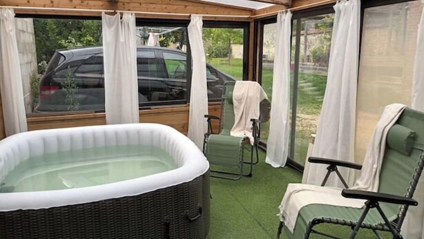 Ein überdachter Außenbereich mit Whirlpool, zwei Stühlen und einem durch die Fenster erkennbaren Auto.